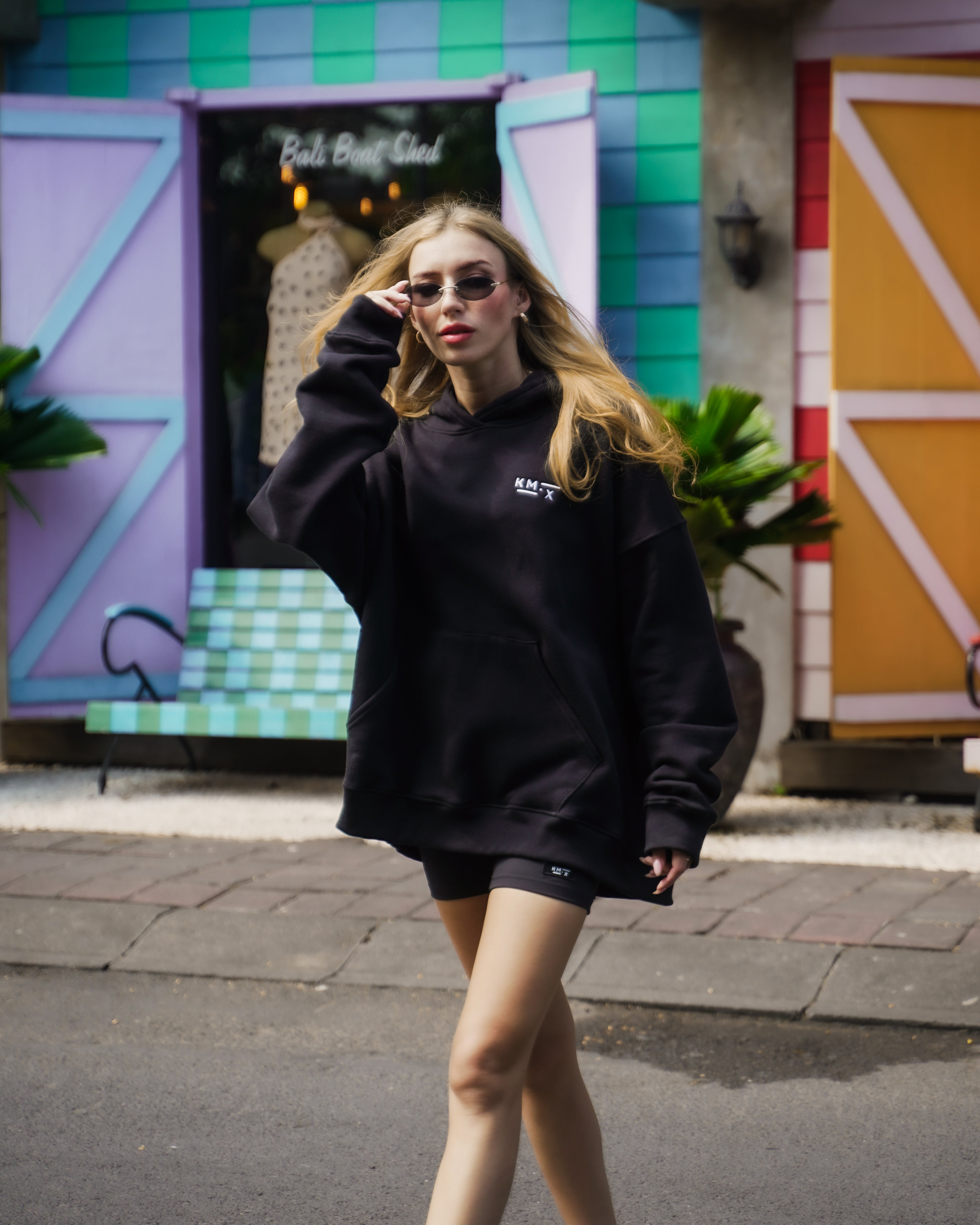 Woman wearing a black KM.X hoodie in front of a colorful building
